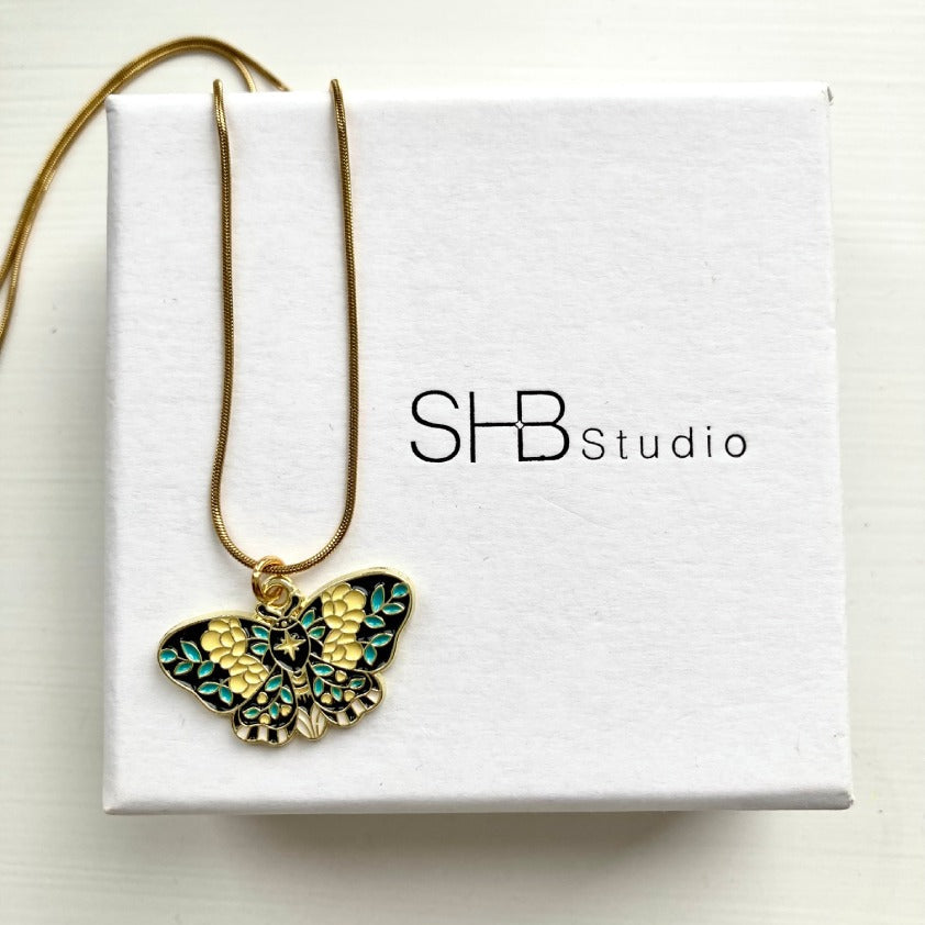Butterfly-shaped pendant necklace on a box with 'SHB Studio' branding.