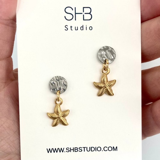Starfish-shaped earrings with gold and silver details on a white card with SHB Studio branding.