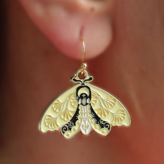 A gold-colored moth earrings with intricate details, displayed on a person's ear.