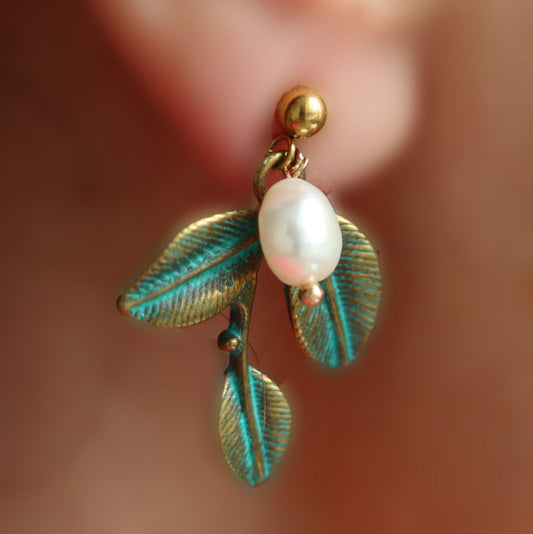 A single pearl earring with a gold-colored leaf design and a hypoallergenic round ball stud.