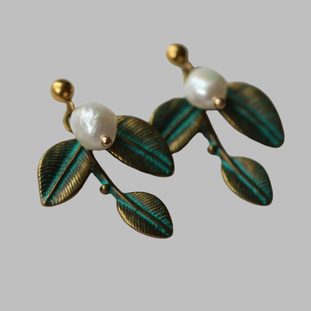 Pair of earrings with leaf design and pearl-like beads on a Shob Studio branded card.