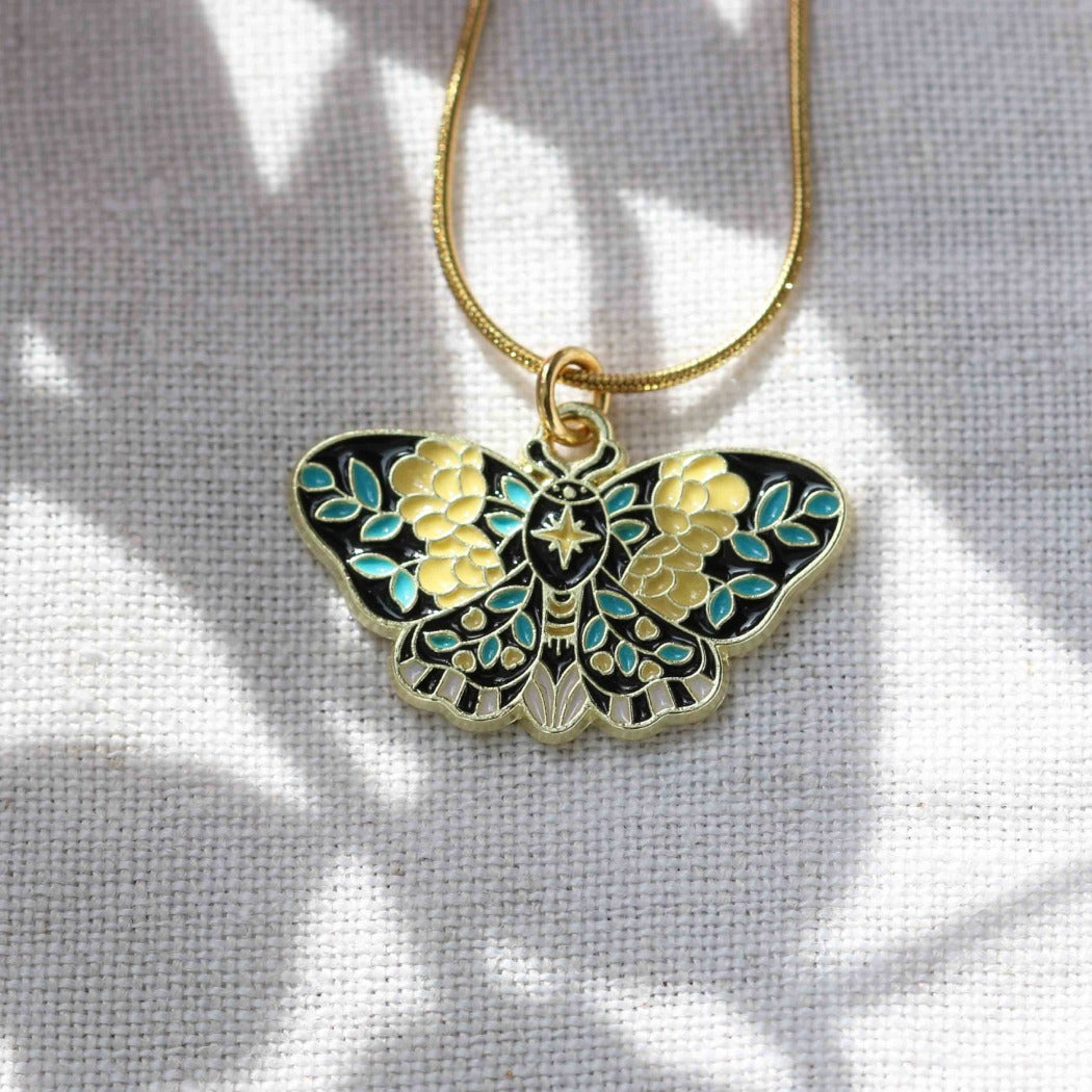 Butterfly-shaped pendant on a gold chain against a light gray background