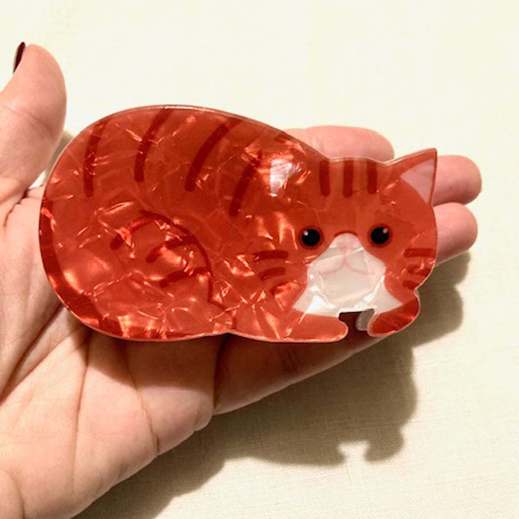 orange-cat-shaped hair clip held in a hand against a beige background
