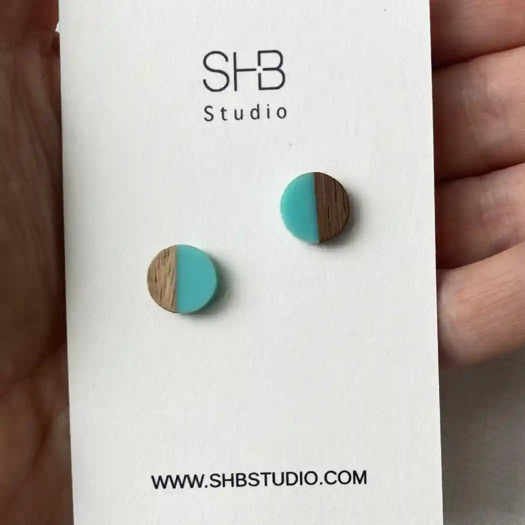 Turquoise and wood round earrings on a SHB Studio card held by a hand.