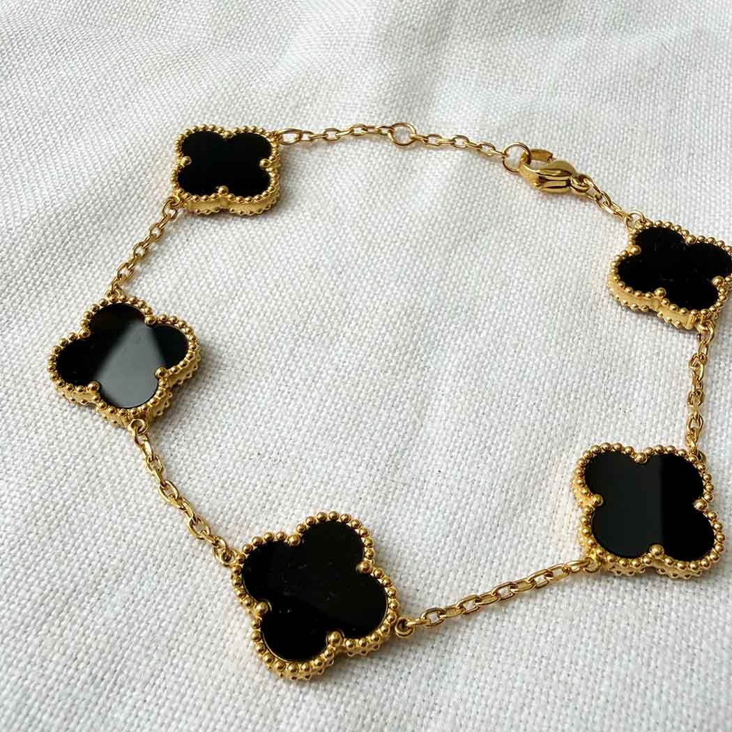 Gold necklace with black clover-shaped pendants on a white fabric background