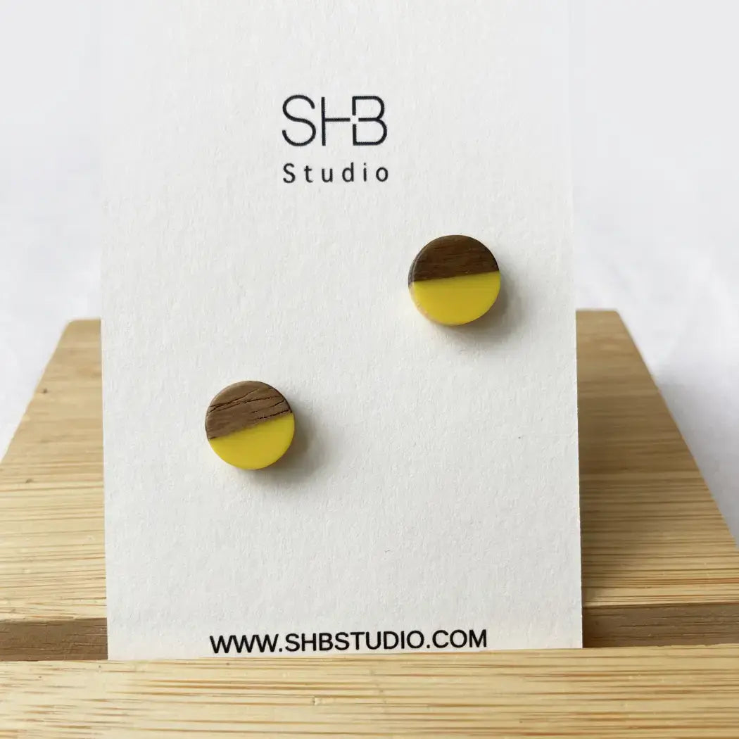 Wooden earrings with yellow and brown design on a white card with SHB Studio branding.