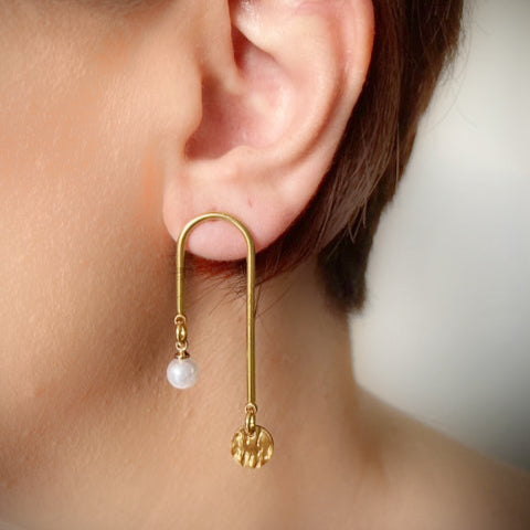 A close-up image of a woman's ear wearing a gold-colored U-shaped earring with a pearl embellishment.