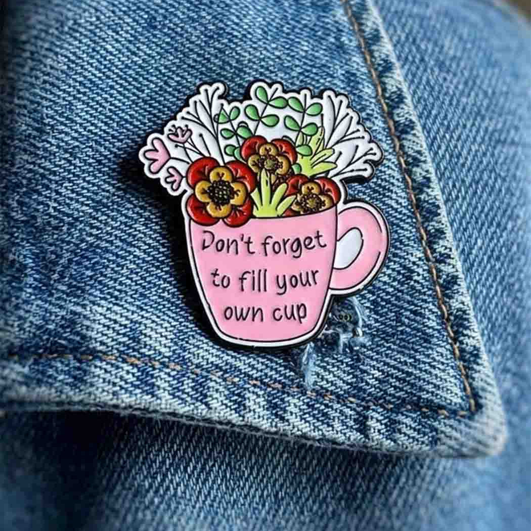 Pink enamel pin badge illustrated with a cup and flowers, reading 'Don't forget to fill your own cup.