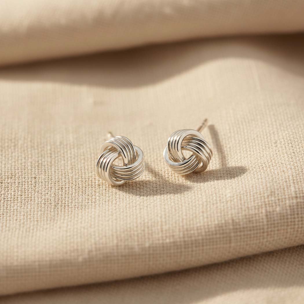 Knot sterling silver studs display on cream fabric..