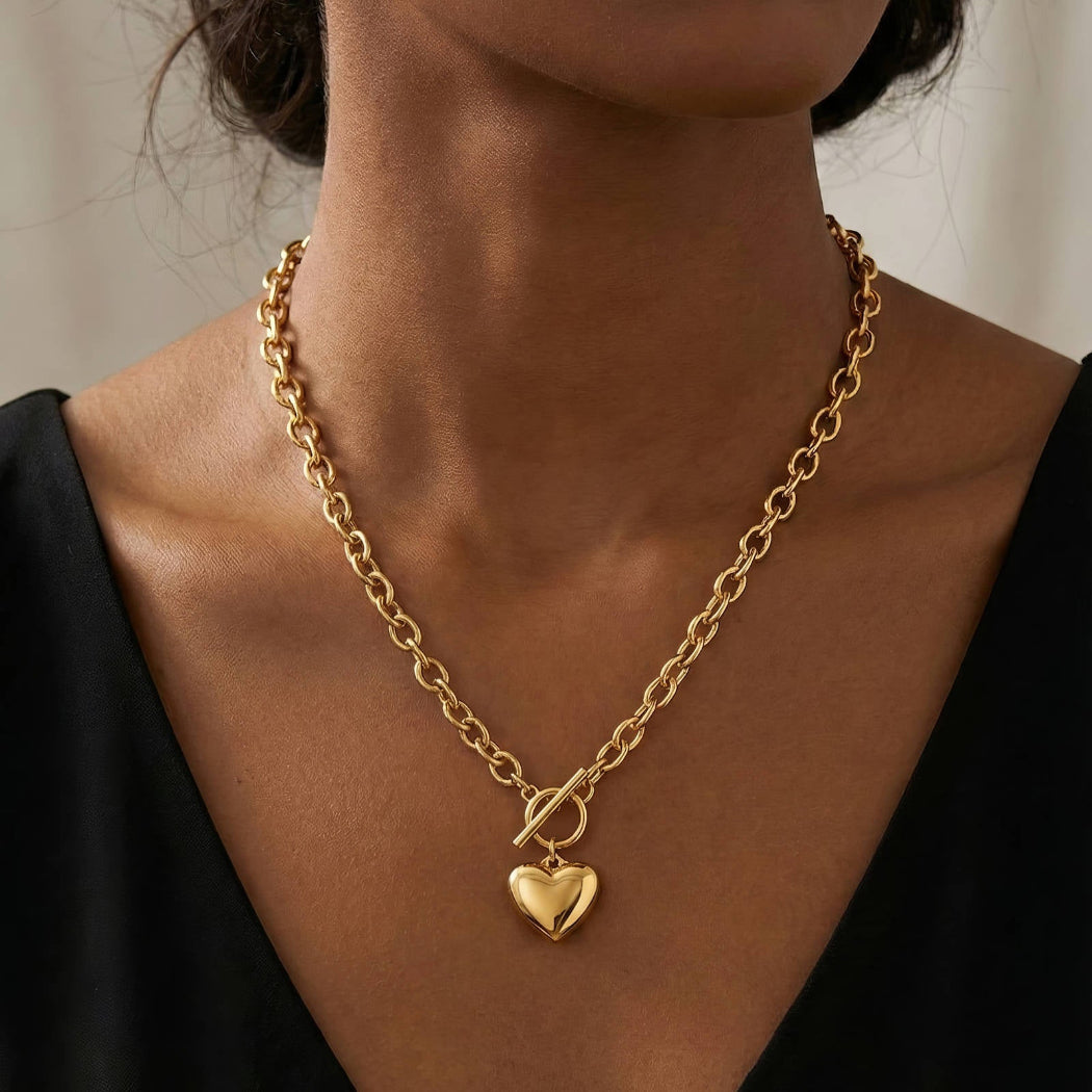 Gold chain necklace with a heart pendant worn by a person against a neutral background