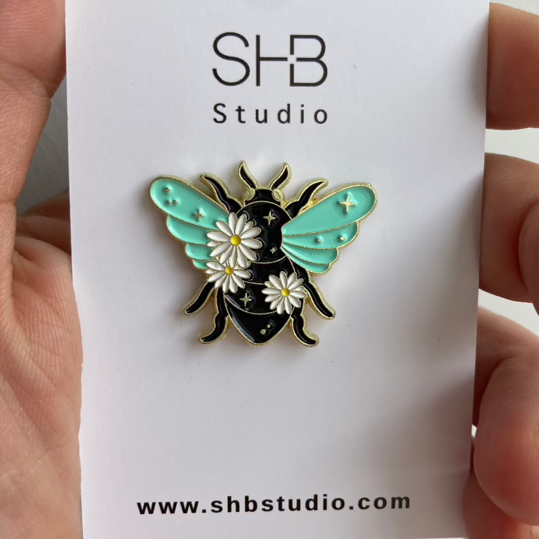 Mint and gold celestial bee enamel pin with daisies and stars on a black body — small meaningful gift from SHB Studio.