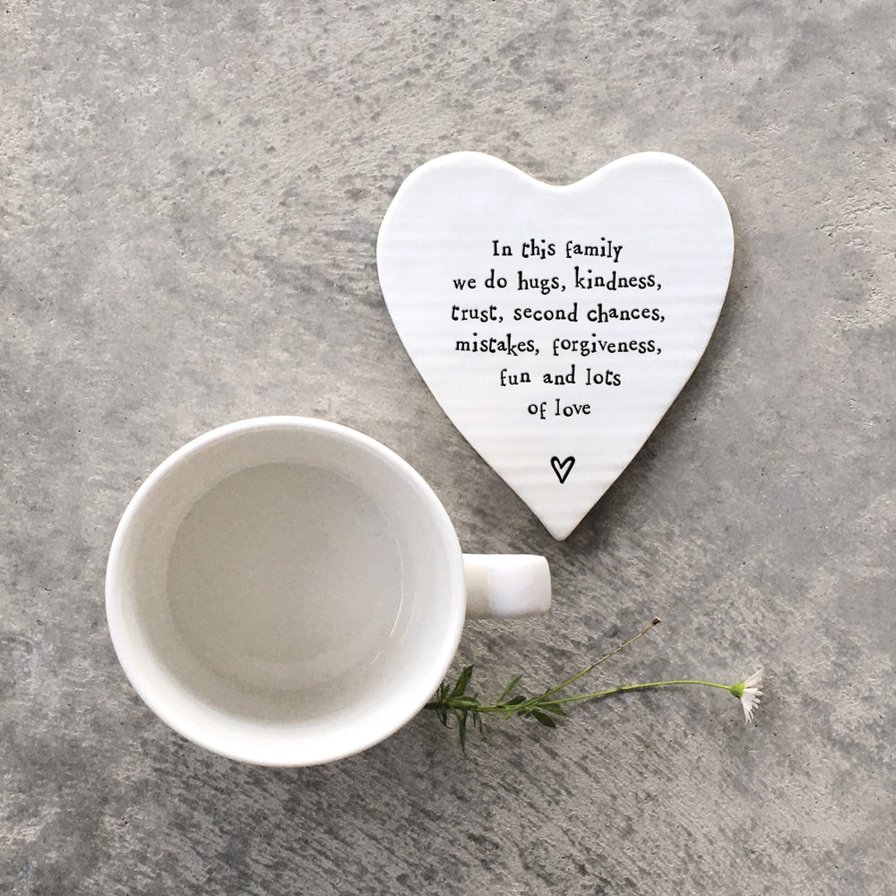 Heart-shaped porcelain coaster with text and a white mug on a gray surface