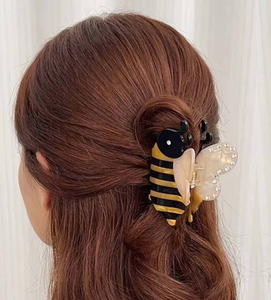 Hair accessory shaped like a bee with a butterfly on brown hair against a white background