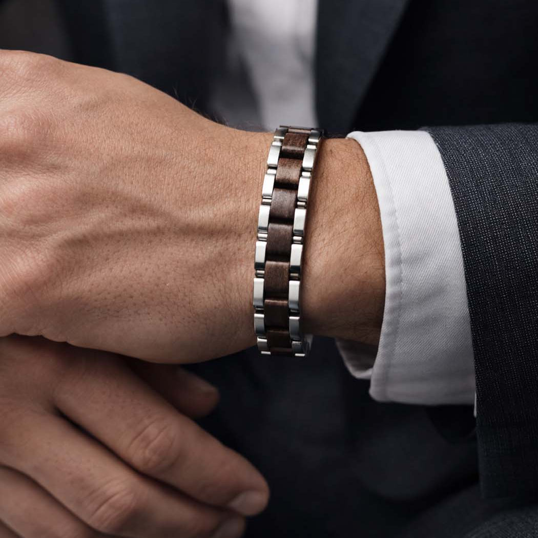 Close-up of a person wearing a silver and brown bracelet on a dark suit sleeve.