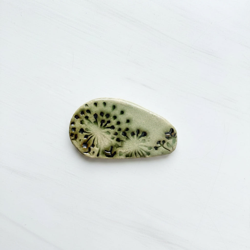 ceramic  brooch piece with black patterns on a white card with SHB Studio branding.
