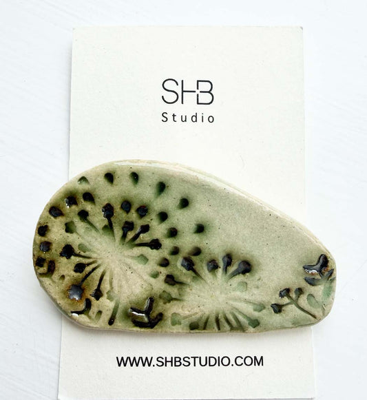 ceramic  brooch piece with black patterns on a white card with SHB Studio branding.