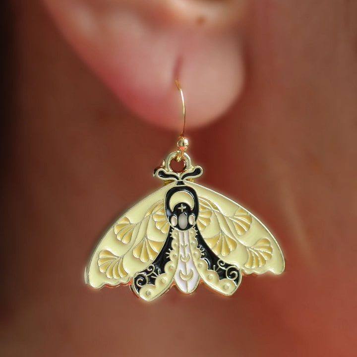 A gold-colored moth earrings with intricate details, displayed on a person&