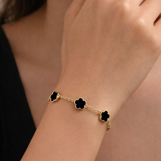 Close-up of a woman’s hand wearing a gold bracelet with three black clover charms.