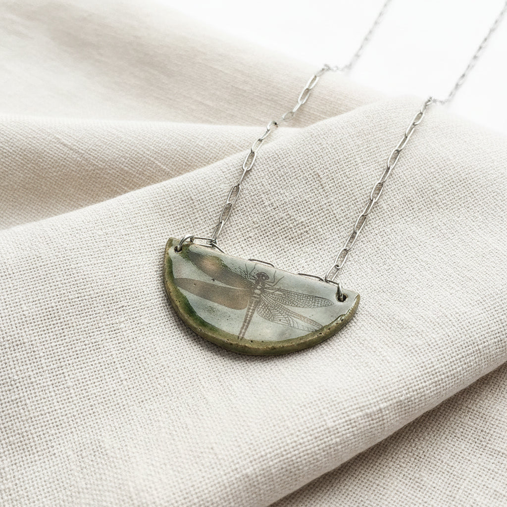 Necklace with a half-circle pendant featuring a dragonfly design on a white background