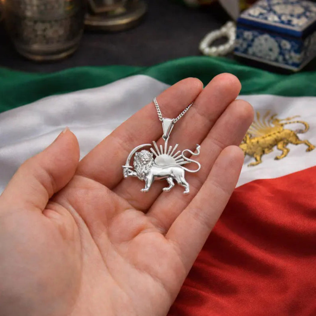 Silver lion pendant necklace held in a hand with a flag in the background