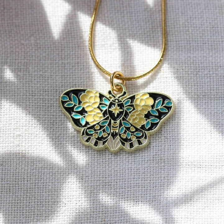 Butterfly-shaped pendant on a gold chain against a light gray background