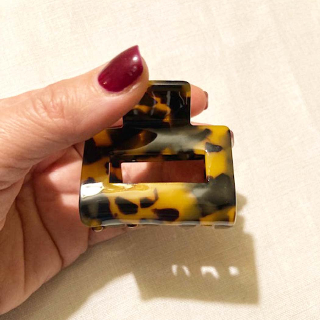 Hand holding a tortoiseshell patterned hair claw against a beige background
