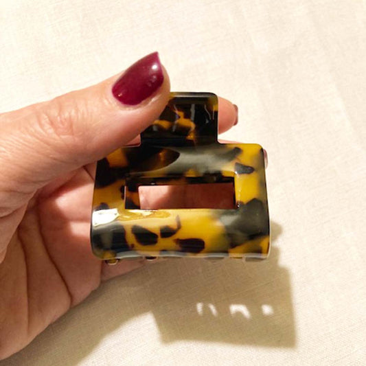 Hand holding a tortoiseshell patterned hair claw against a beige background