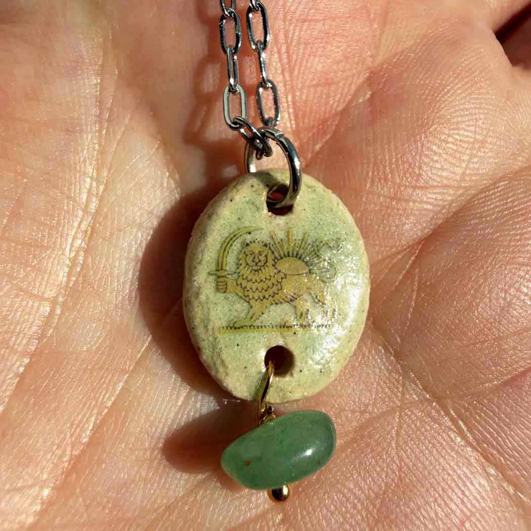 Necklace with a grreen gemstone pendant featuring a lion and sun held in a hand.