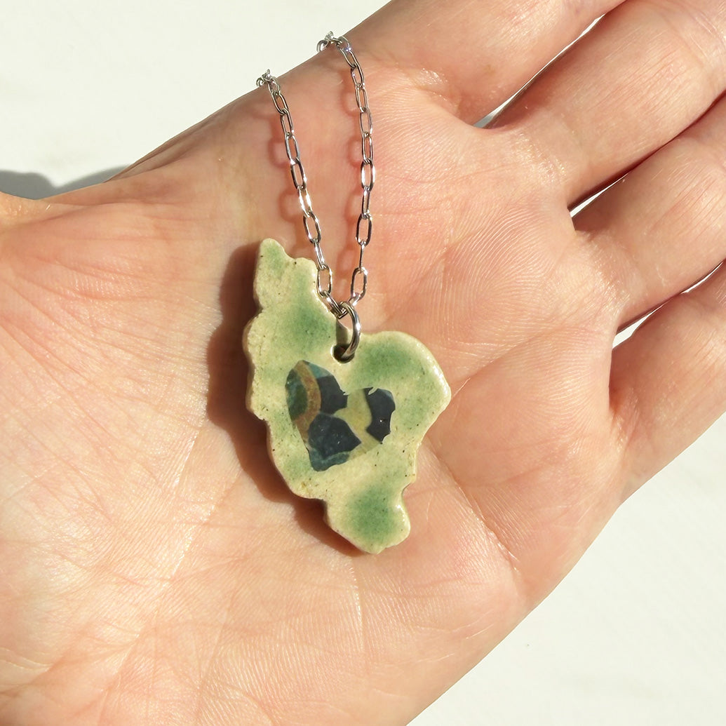 Hand holding a green ceramic Iran map pendant with a chain