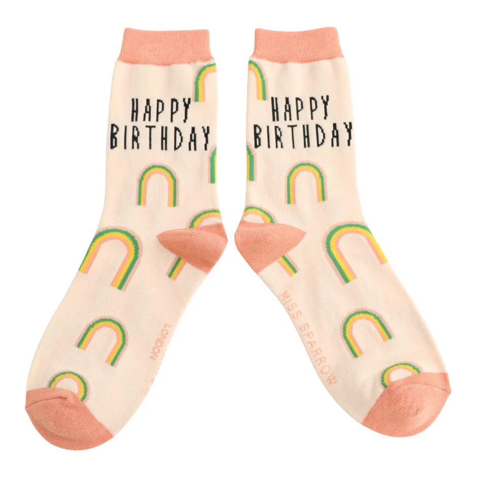 Pair of socks with 'Happy Birthday' text and rainbow patterns on a beige background