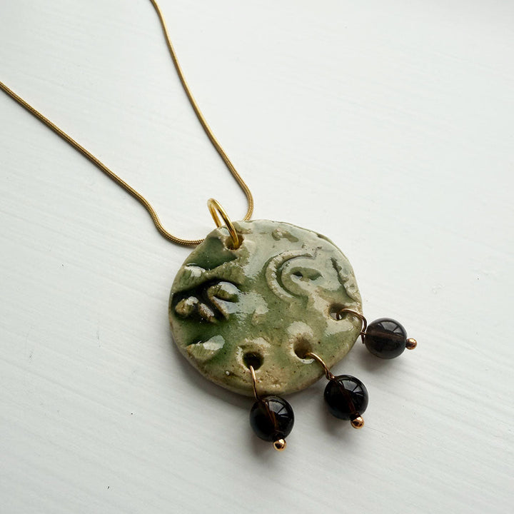 Necklace with a green ceramic pendant and black beads on a white background