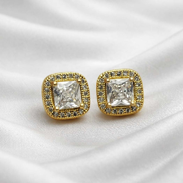 Gold square earrings with clear gemstones on a white satin background