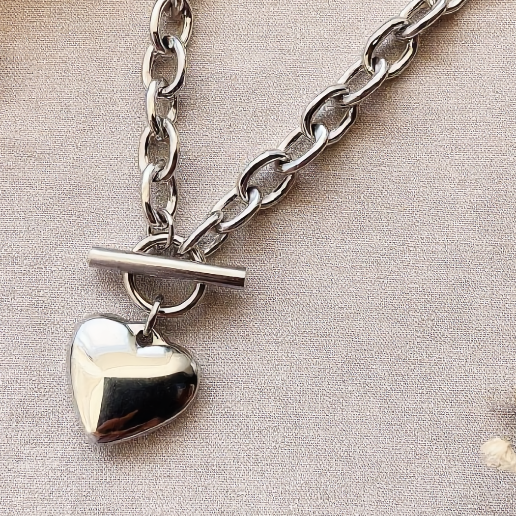 Silver chain necklace with a heart pendant on a beige background with dried flowers.