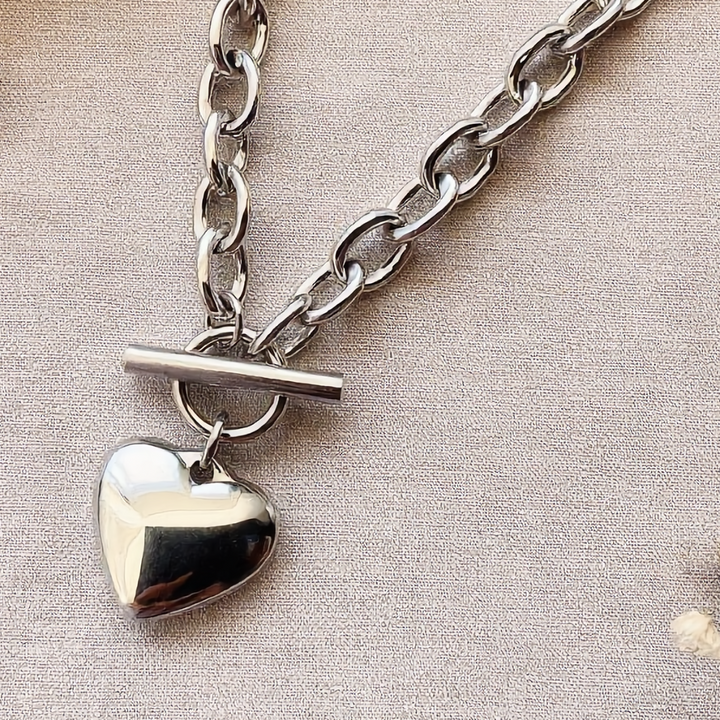 Silver chain necklace with a heart pendant on a beige background with dried flowers.