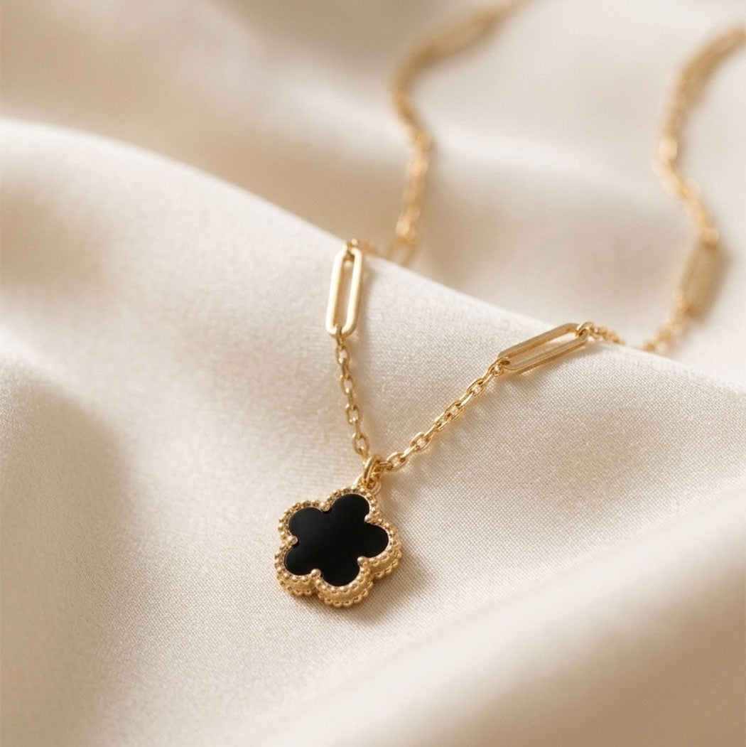 Gold necklace with a black clover pendant on a beige fabric background