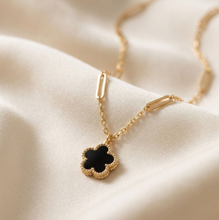 Gold necklace with a black clover pendant on a beige fabric background