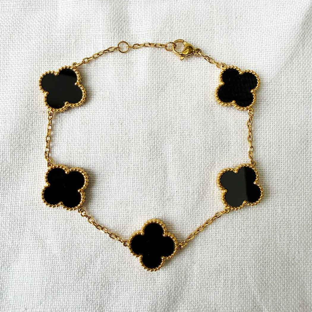 Gold bracelet with black clover-shaped charms on a white background