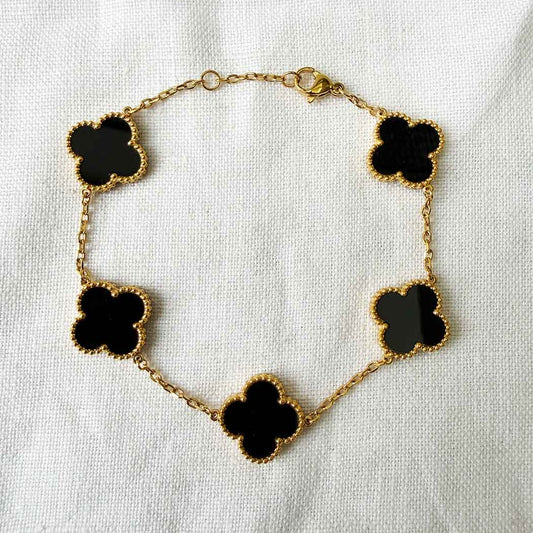 Gold bracelet with black clover-shaped charms on a white background