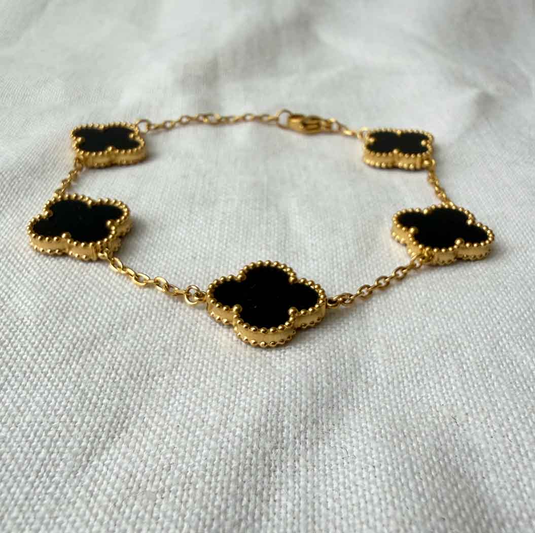 Gold bracelet with black clover-shaped charms on a white fabric background