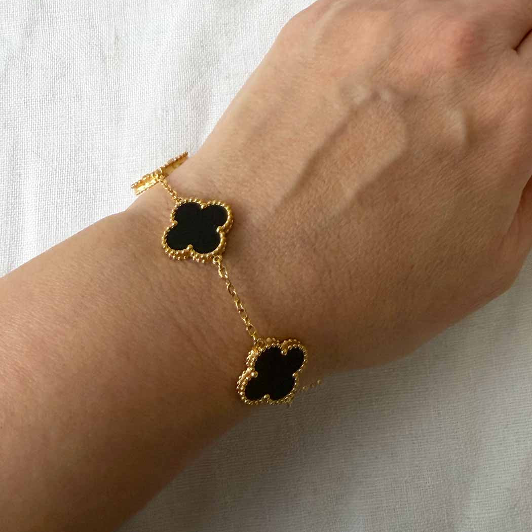 Gold bracelet with black clover charms on a wrist against a white background