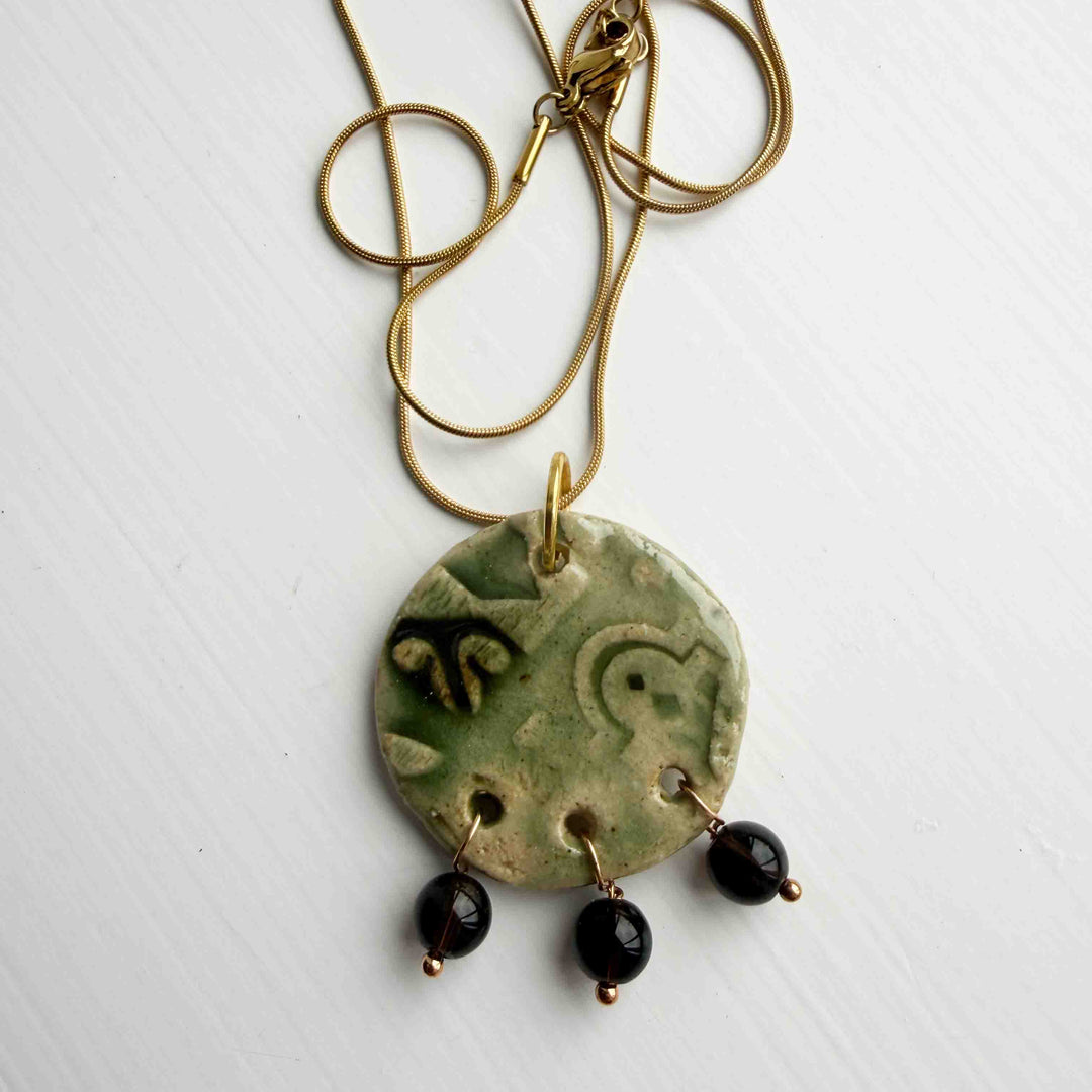 Necklace with a green ceramic pendant and black beads on a white background.1