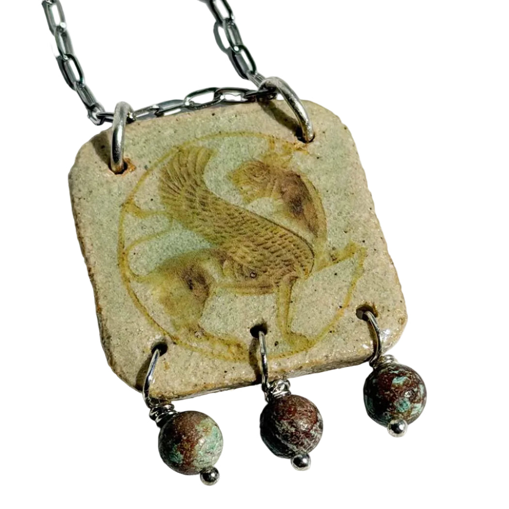 Handmade square ceramic pendant by SHB Studio featuring the Persian Simorgh — a mythological winged bird — in sepia on cream glaze, with three turquoise stone drops on antiqued silver chain.