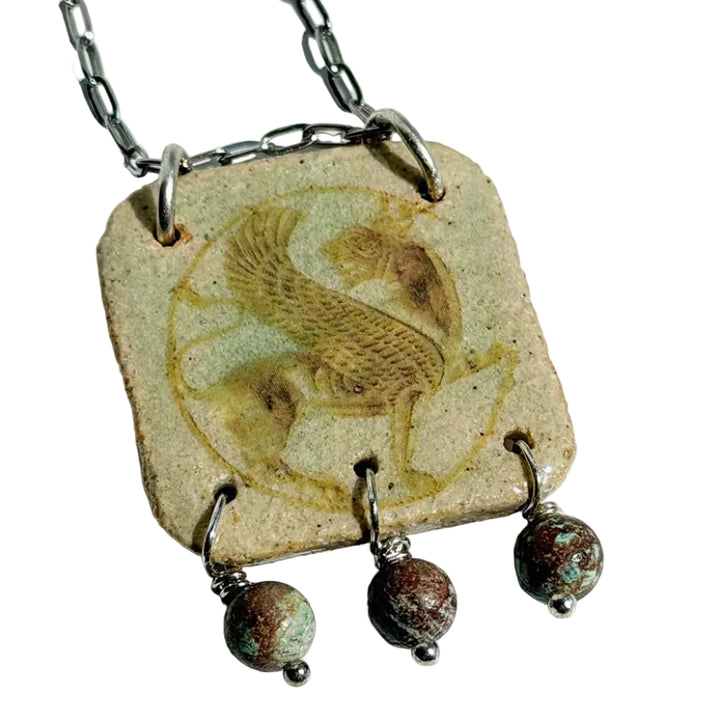 Handmade square ceramic pendant by SHB Studio featuring the Persian Simorgh — a mythological winged bird — in sepia on cream glaze, with three turquoise stone drops on antiqued silver chain.