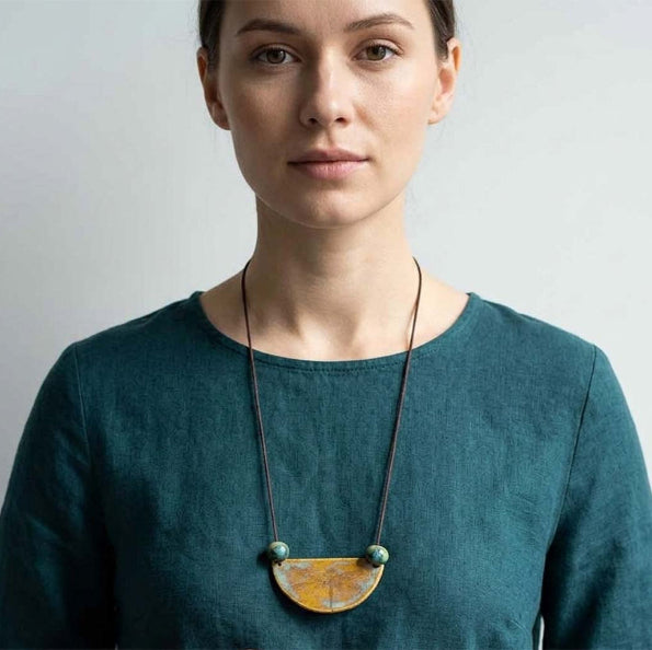 Woman wearing a handmade ceramic necklace with a large pendant against a plain background