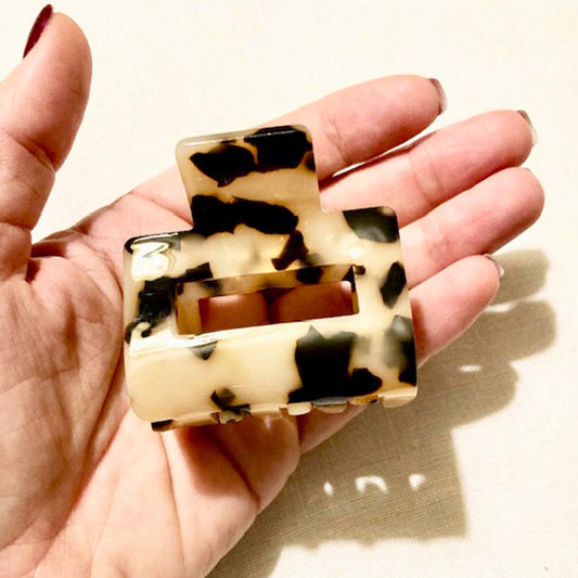 Hand holding a tortoiseshell hair claw against a neutral background