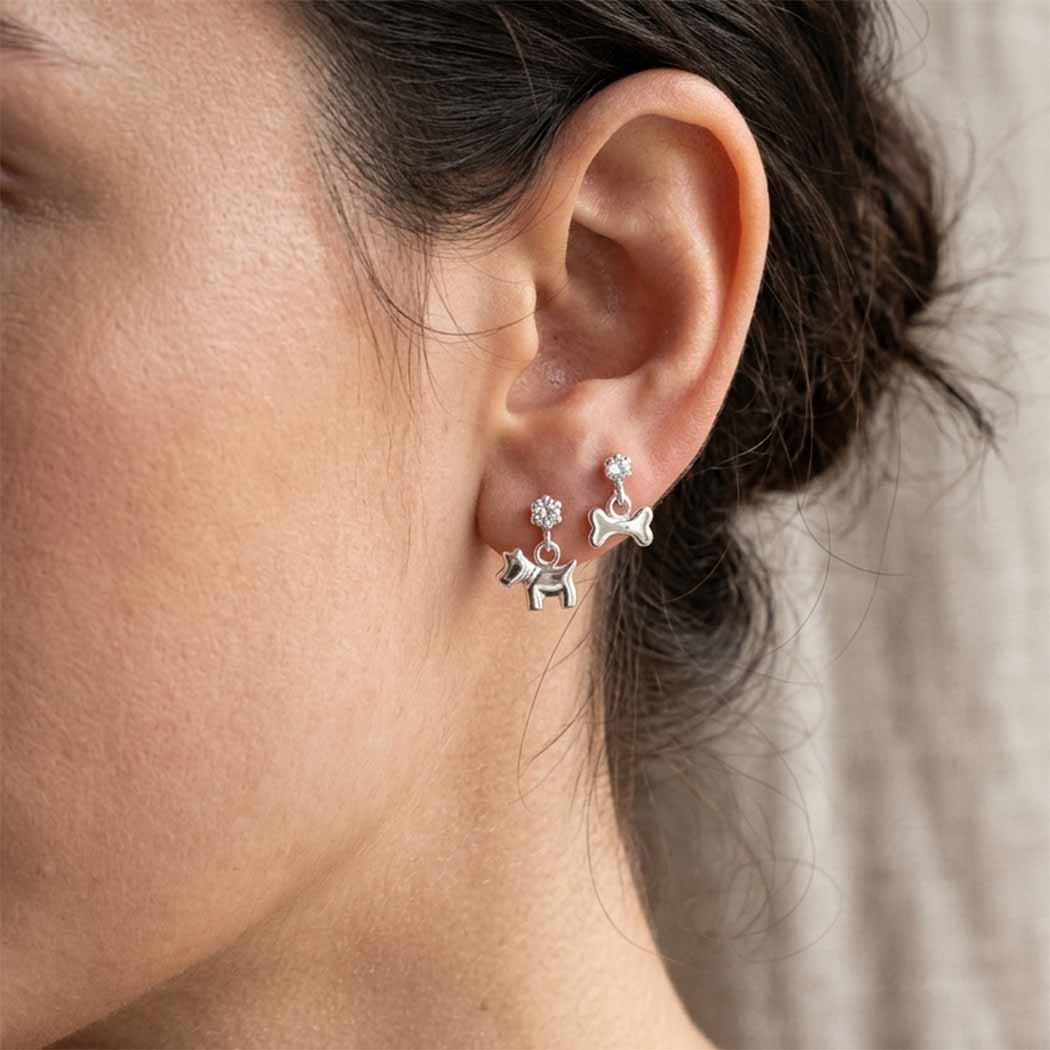 Close-up of an ear wearing silver earrings with dog and bone designs.