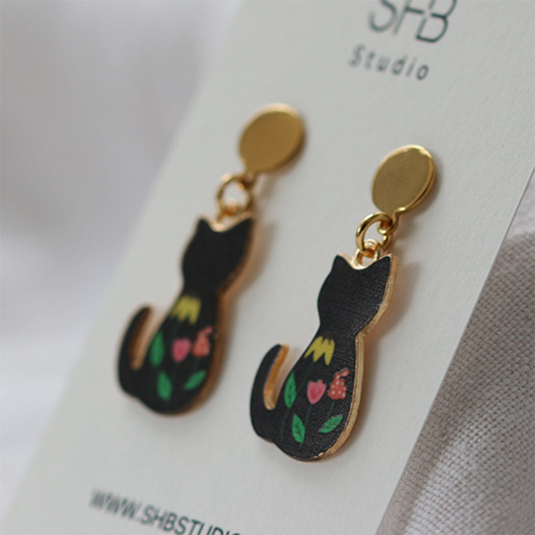 Black cat-shaped earrings with floral designs on a white card with 'SHB Studio' branding.