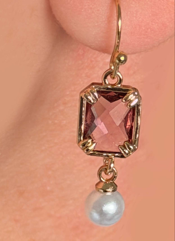Close-up of a light purple crystal glass square earring with a white faux pearl drop and gold hook