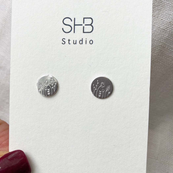 Silver earrings with floral designs on a white card with &