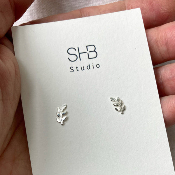 A pair of sterling silver leaf stud earrings displayed on a white card with &